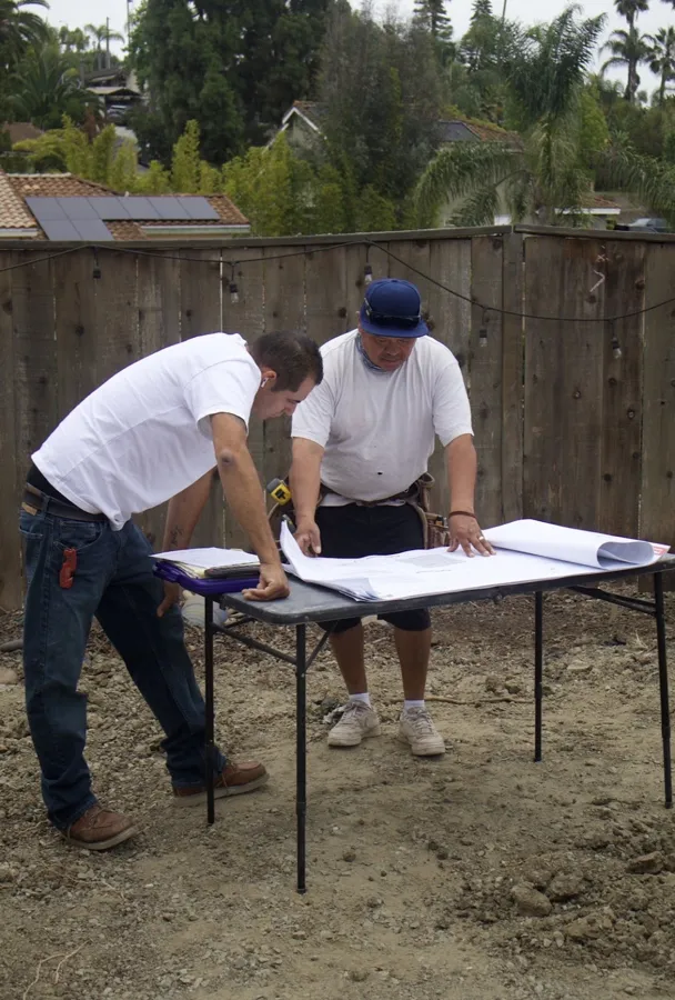 Two crew members going over the plans on a folding table at a backyard job site